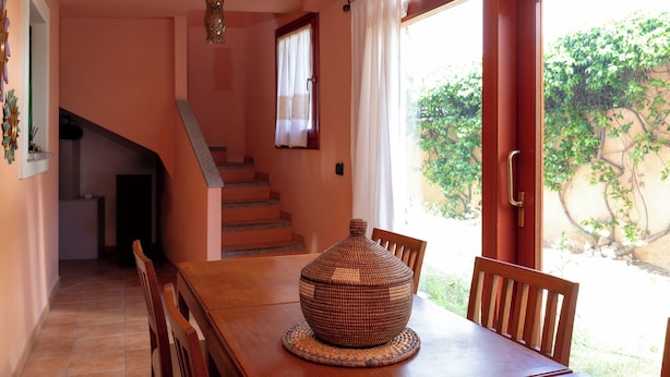 A dining area with a wooden table and chairs, a decorative vase, and a staircase leading to an upper level. - Casa Marzia by Wonderful Italy (Olbia)
