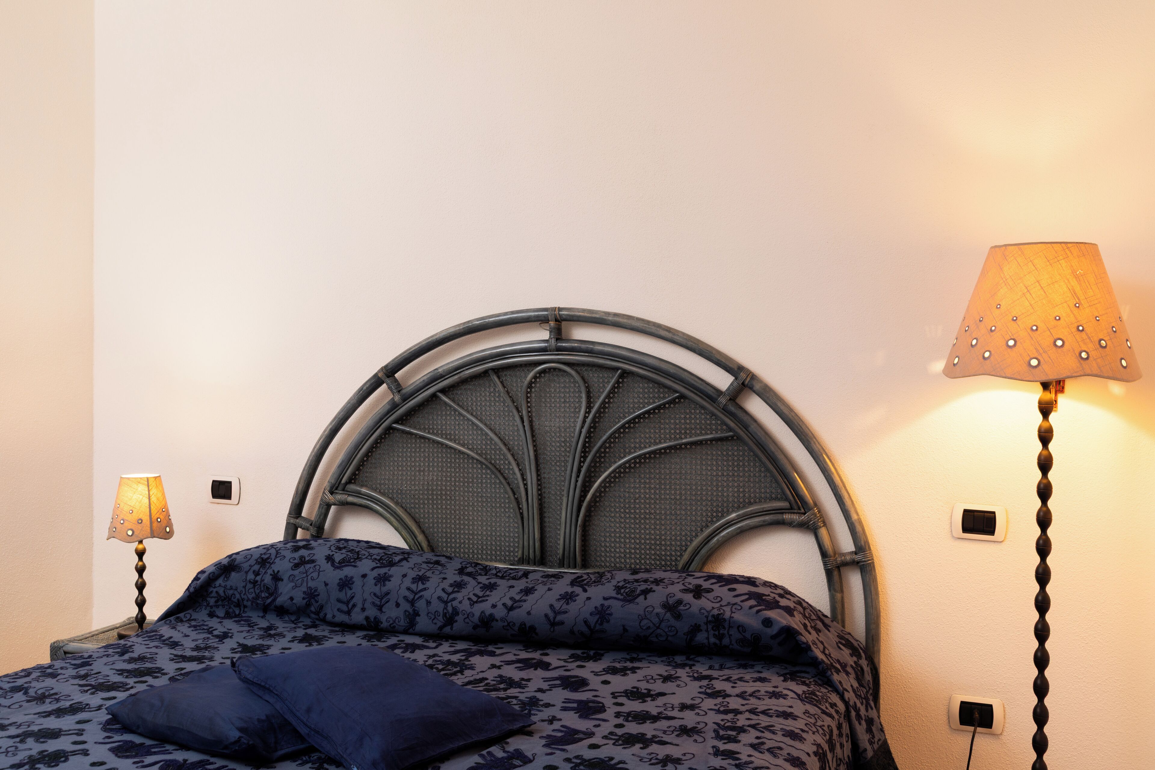 A bed with a metal headboard, two bedside lamps, and a wall socket.