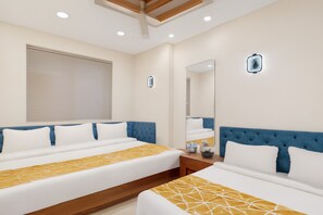 A hotel room with two beds, a large mirror, a bedside table, and a window with a blind.