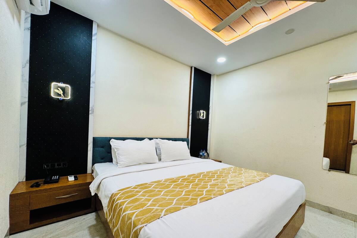 A hotel room with a bed, bedside table, and a mirror.
