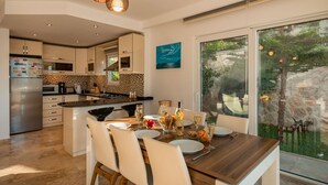 A modern kitchen with a central island, a dining area with a view of the outdoors, and a large window.