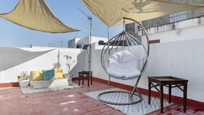 Eine Dachterrasse mit Hängesessel, einem kleinen Tisch und einer Couch mit Kissen.