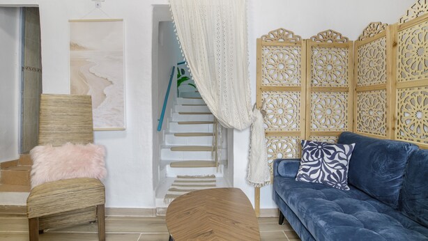 Ein Wohnzimmer mit einem blauen Sofa, einem Holzstuhl mit flauschigem Kissen, einem Holztisch, einer Treppe und einem dekorativen Holzpaneel.