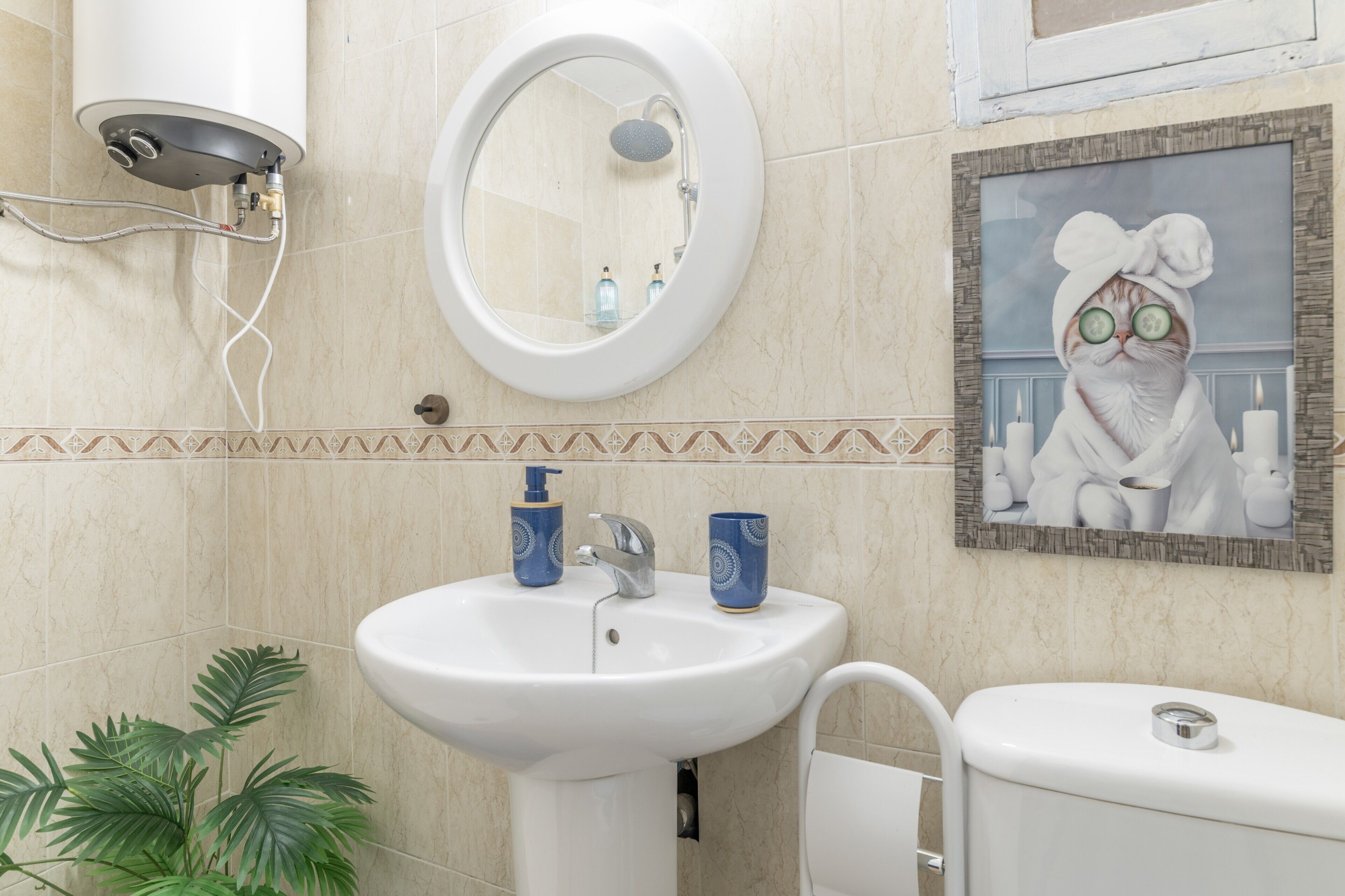 Un bany amb un lavabo, mirall, vàter i un quadre amb marc a la paret.