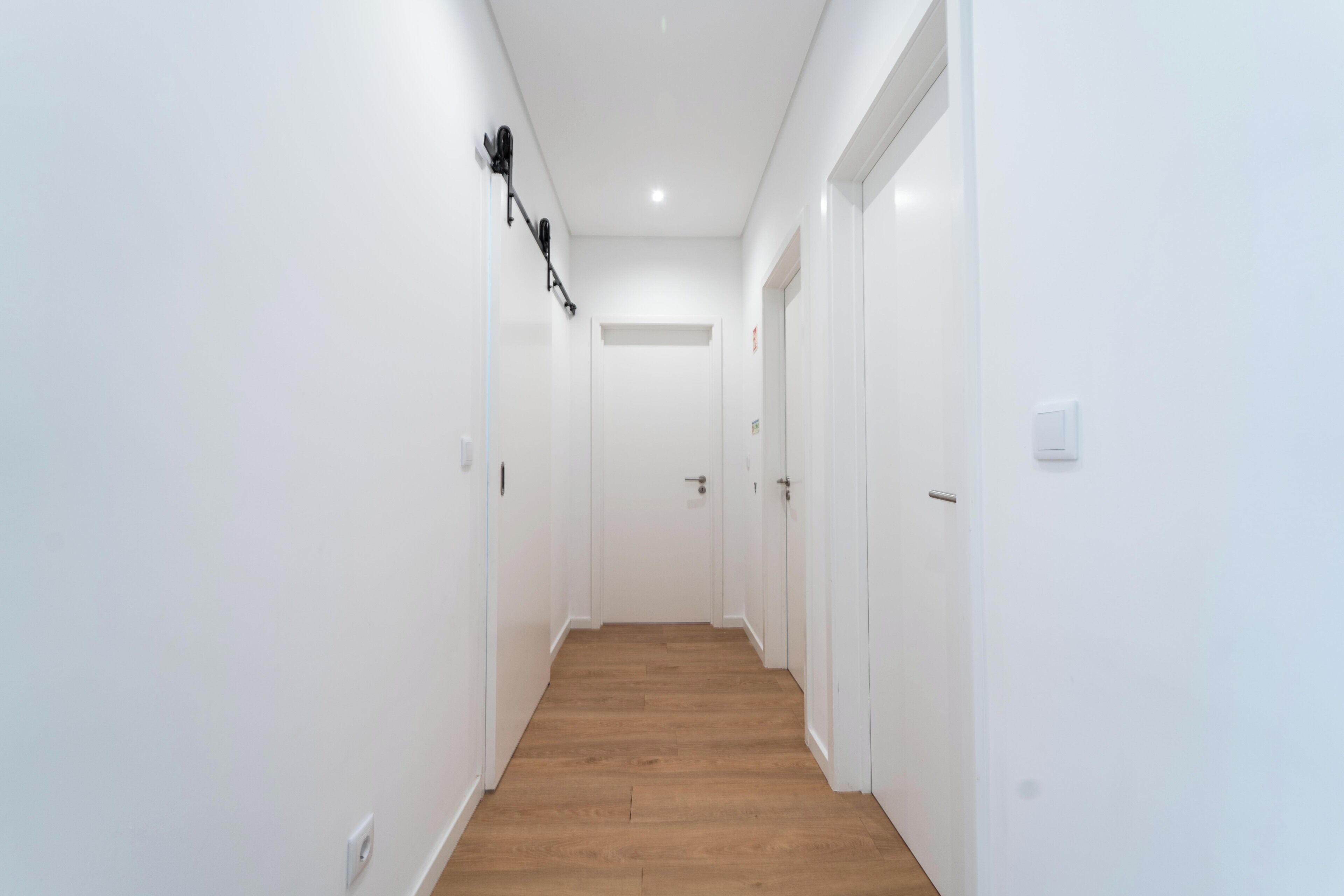 A narrow, white-walled hallway with wooden flooring and a ceiling light.
