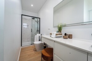 A modern bathroom with a glass shower enclosure, a white sink, and a wooden floor. - Auréa House - Luxury with an Ocean View (Ponta Delgada)