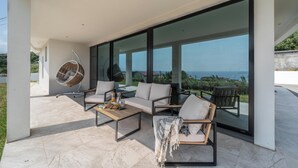 Ein moderner Außenbereich zum Sitzen mit einer Couch, Stühlen und einem Hängesessel, mit Blick auf eine schöne Aussicht.