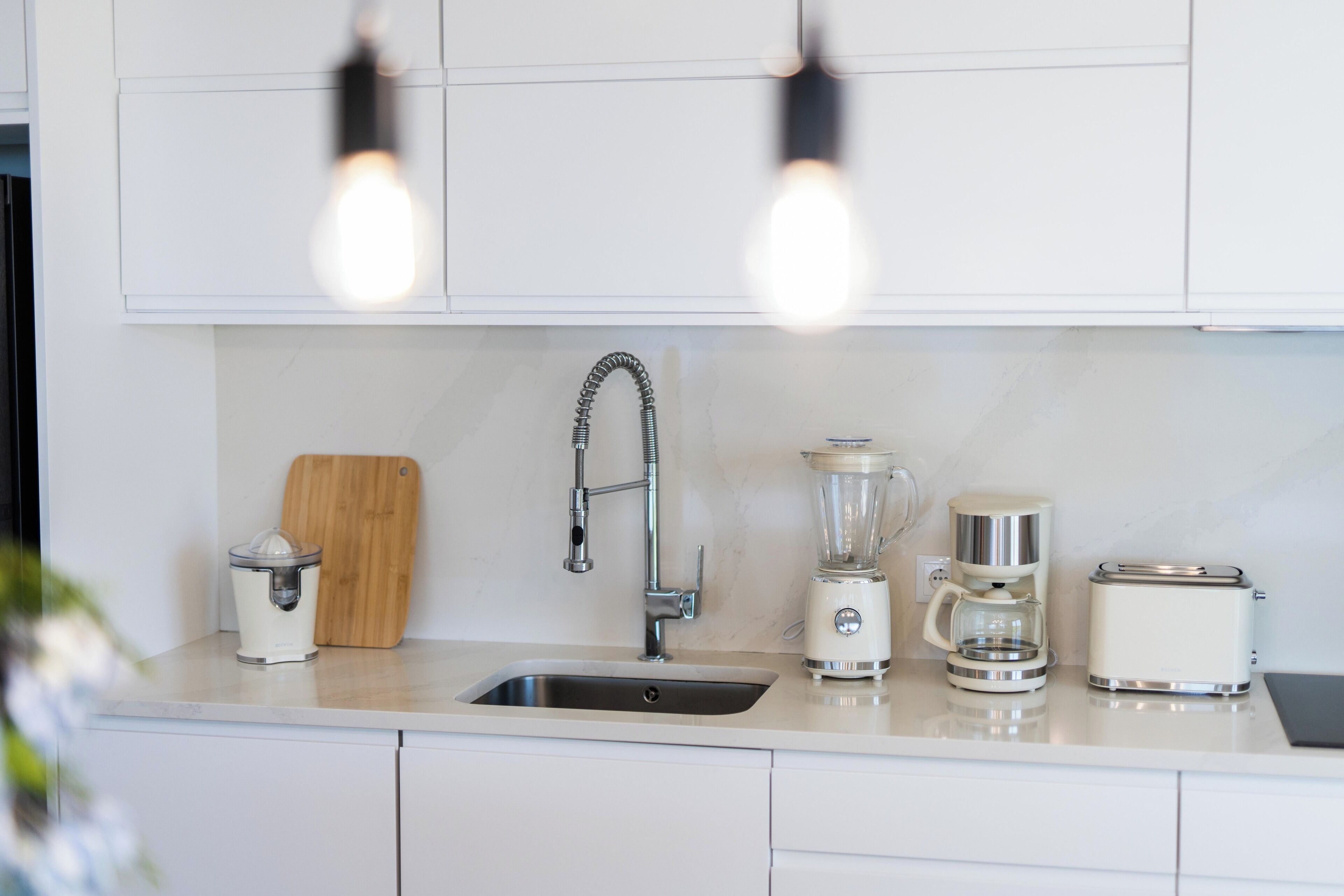 A modern kitchen with a sink, a coffee maker, a blender, and a toaster on the counter.