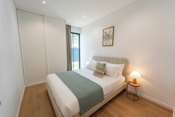 A bedroom with a bed, a bedside lamp, a window, and a painting on the wall.
