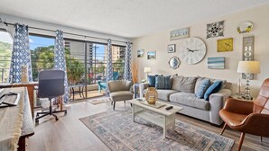 A spacious living room with a large window, a grey sofa, a coffee table, and a brown leather chair. - Charming condo close to the beach! Ocean Villas 101 (Myrtle Beach)