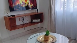 A living room with a TV mounted on the wall, a round coffee table with a plant, and a patterned rug.