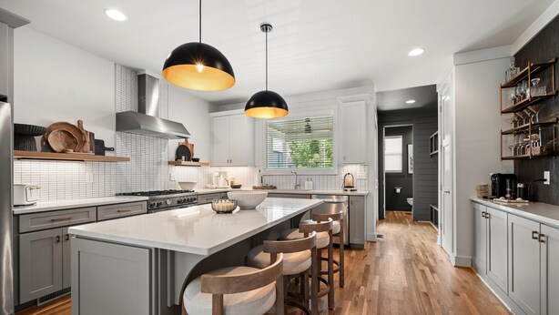 A modern kitchen with a large island, bar stools, pendant lighting, and wooden flooring. - New Stunning 4BR Nashville Home | Rooftop • Shuffleboard • Mural • Designer Interiors (Nashville)