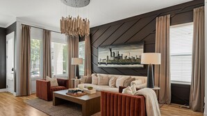 A modern living room with a sofa, coffee table, and two side tables. There is a painting on the wall and a window with curtains. - New Stunning 4BR Nashville Home | Rooftop • Shuffleboard • Mural • Designer Interiors (Nashville)