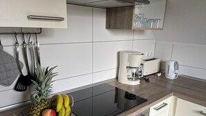 A kitchen with a black induction cooktop, a coffee maker, and a kettle. There is a fruit basket with apples and bananas on the counter. - Cozy vacation apartment with terrace and sauna (Röbel)