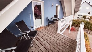 A wooden deck with two black chairs and a table, a white railing, and a blue wall. - Cozy vacation apartment with terrace and sauna (Röbel)