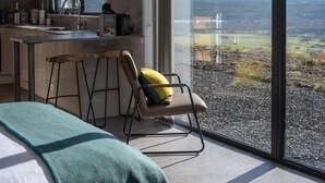 A modern kitchen with a large window, a bar stool, and a view of a rural landscape. - Migdale Heights - Luxury Cabins in The Highlands (Ardgay)