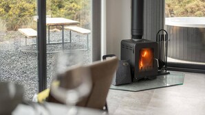 A modern interior with a wood-burning stove, a glass table, and a view of the outdoors. - Migdale Heights - Luxury Cabins in The Highlands (Ardgay)