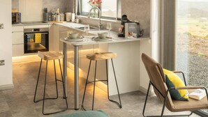 A modern kitchen with a bar area, a TV, and a view of the outdoors. - Migdale Heights - Luxury Cabins in The Highlands (Ardgay)