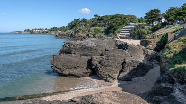 A coastal landscape with rocky cliffs, a beach, and a staircase leading up to a building. - Seafront, apartment for 4 people (Pornic)