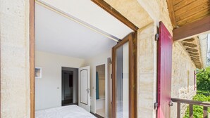 A bedroom with a bed, a wooden door, and a view of greenery outside.