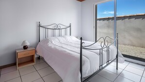 Een slaapkamer met een metalen bed, witte beddengoed, een nachtkastje met een lamp en uitzicht op een balkon door een schuifdeur.