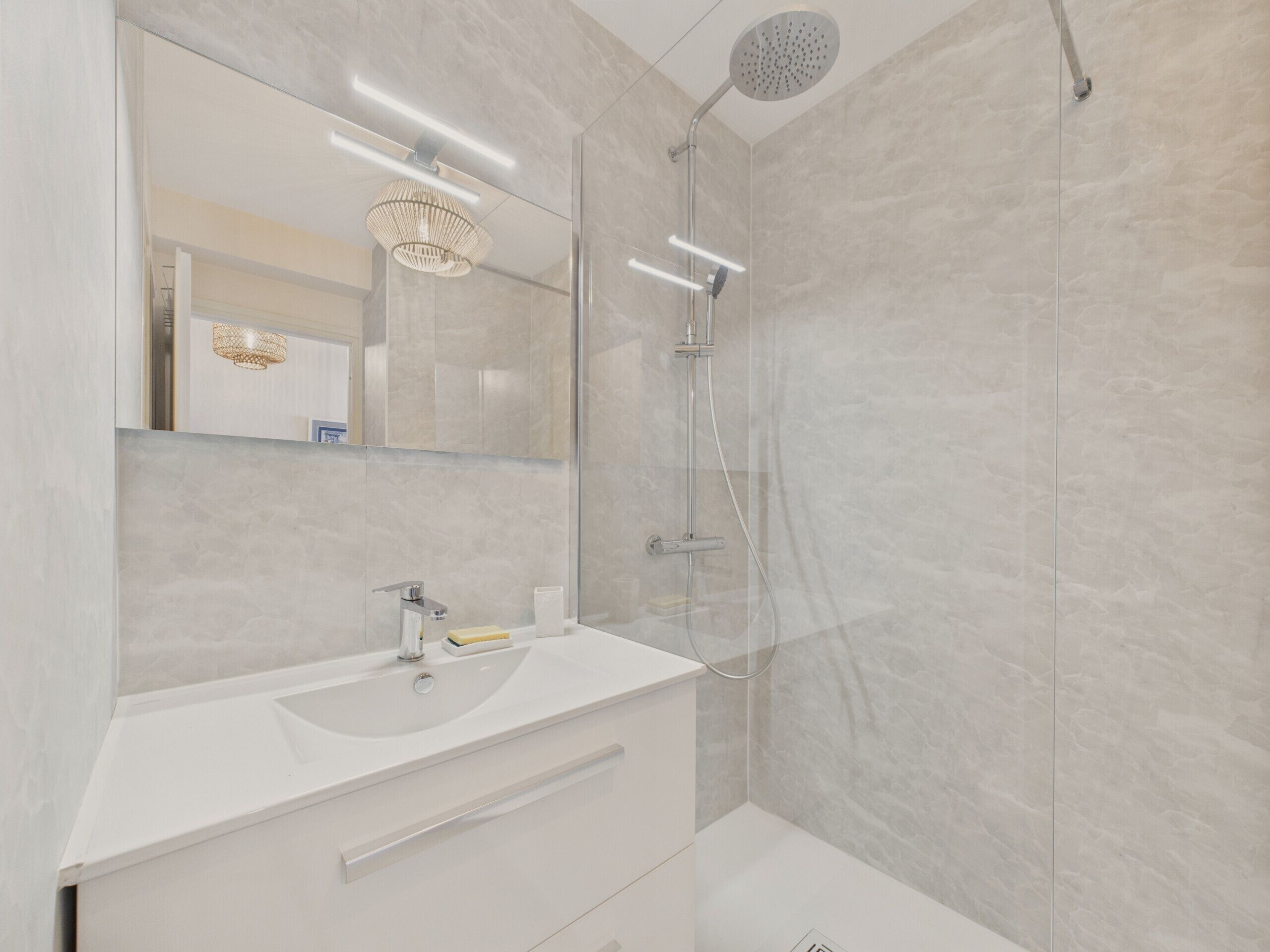 Un baño moderno con lavamanos, espejo y ducha blancos.