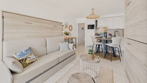A modern living room with a sofa, a round coffee table, and a dining area with a table and chairs. - Sea view,  studio for 4 just 40m from the beach (Les Sables-d´Olonne)