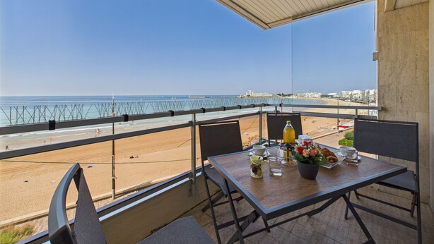 A balcony with a table set for two, overlooking a beach and the sea. - Sea view,  studio for 4 just 40m from the beach (Les Sables-d´Olonne)