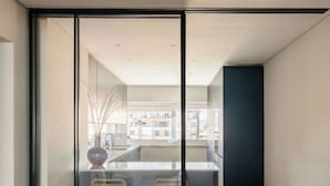 A modern kitchen with a glass partition, wooden flooring, and a view of the cityscape.
