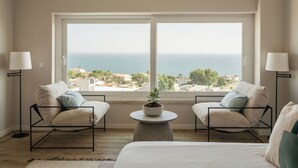 A bedroom with a large window, two armchairs, a round coffee table, and a bed.