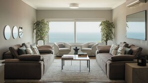 A modern living room with two sofas, a coffee table, and a large window offering a view of the ocean.