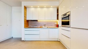 A modern kitchen with white cabinets, a wooden backsplash, and a built-in oven. - Mika's 2-Bedroom Seaview Flat & Parking (Split)