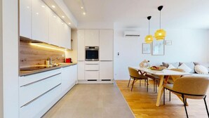 A modern kitchen with white cabinets, a built-in oven, and a dining area with a wooden table and chairs. - Mika's 2-Bedroom Seaview Flat & Parking (Split)