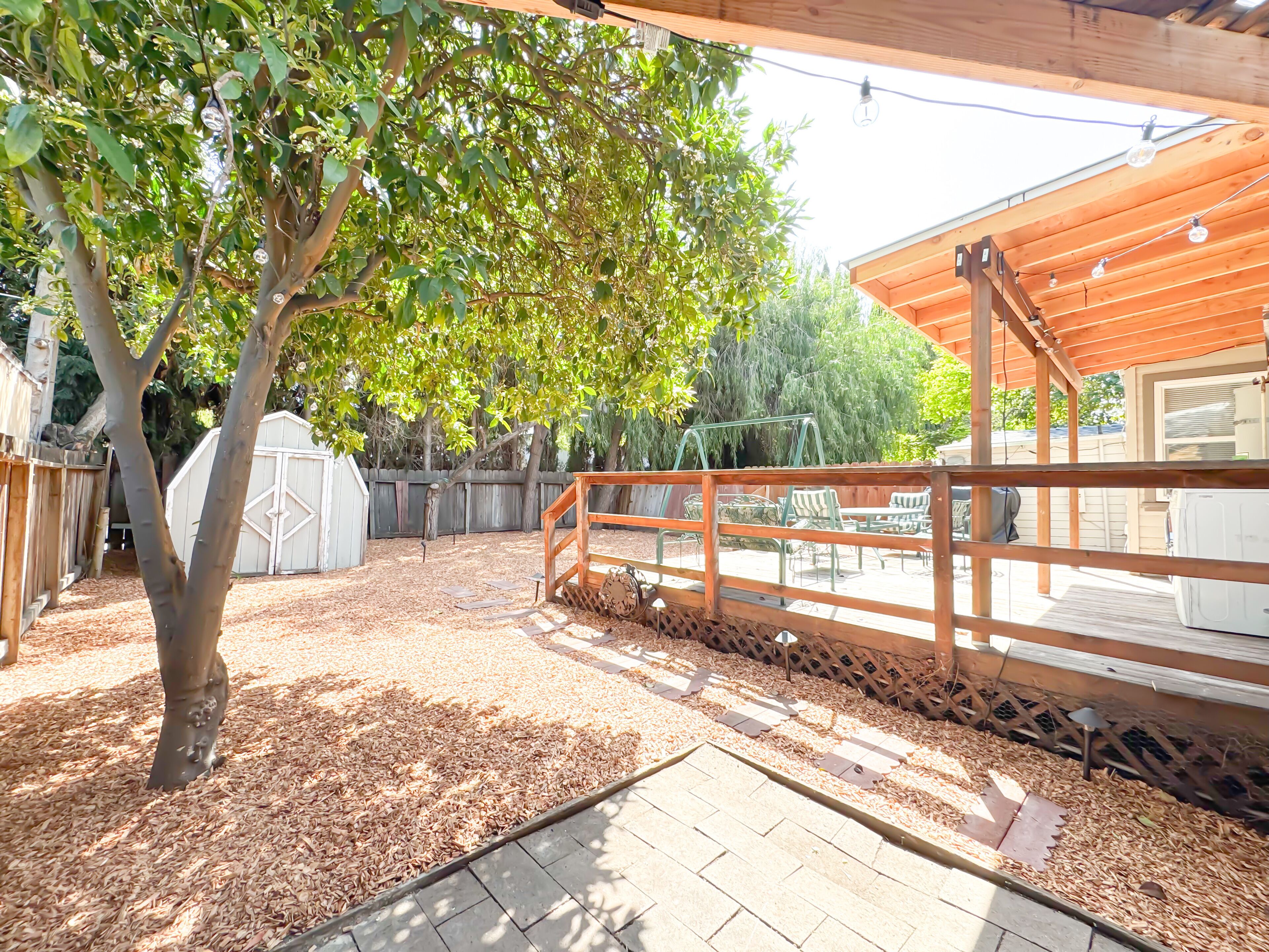A covered patio area with a wooden deck, a swing set, and a fenced play area.