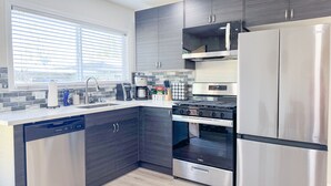 A modern kitchen with dark cabinetry, stainless steel appliances, a dishwasher, and a window with blinds. - Walk to Google 3BR Home Yard & Kitchen (Mountain View)