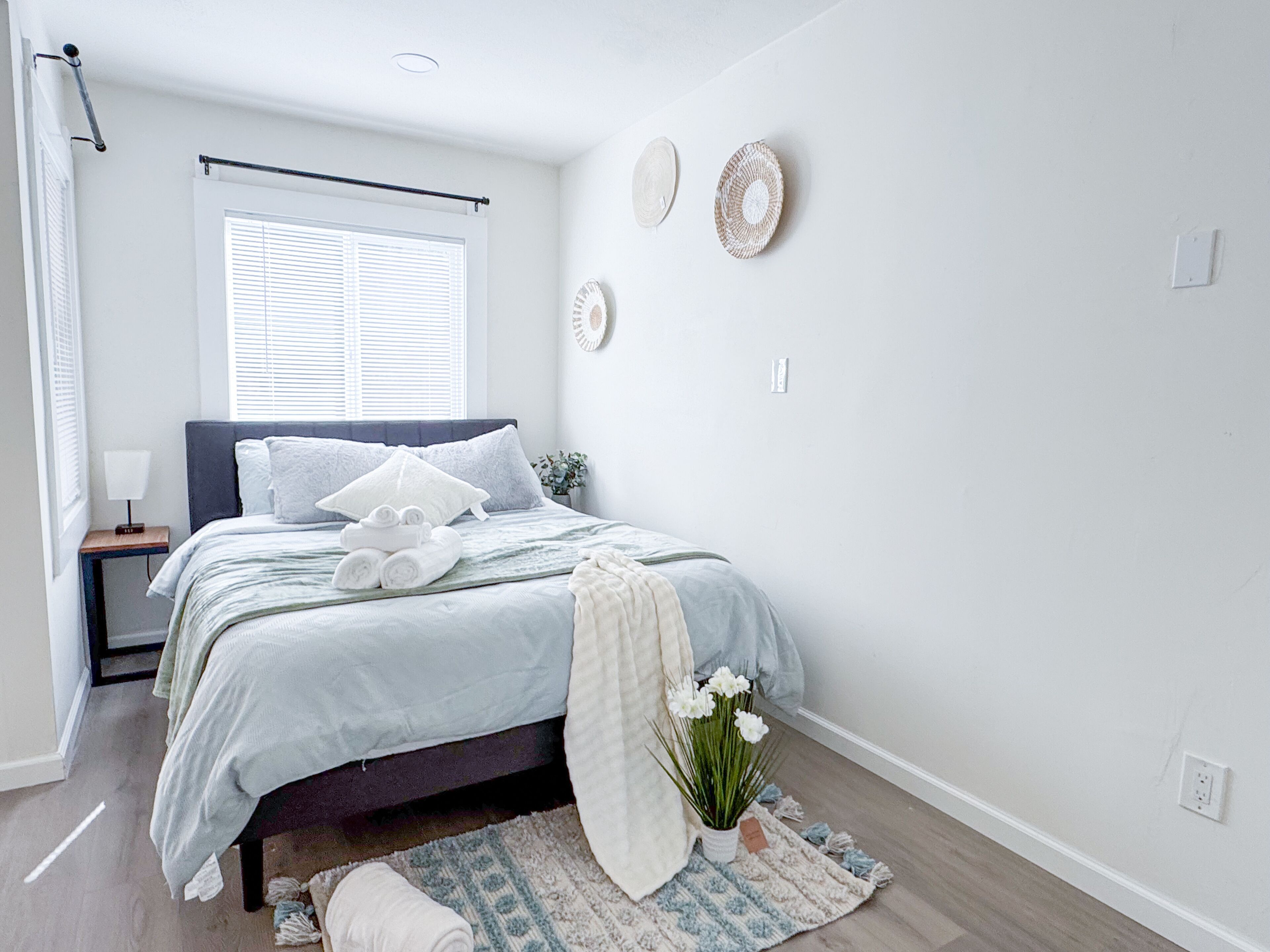 A neatly arranged bedroom with a bed, bedside table, and a window with blinds.