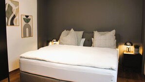 A modern bedroom with a large bed, two bedside tables with lamps, and abstract wall art.