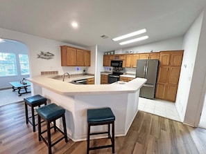 A modern kitchen with a central island, wooden cabinets, stainless steel appliances, and a bar area with stools. - DeStoto Canal Oasis w/ Boat Lift. Walk to Beach! (St. Augustine)