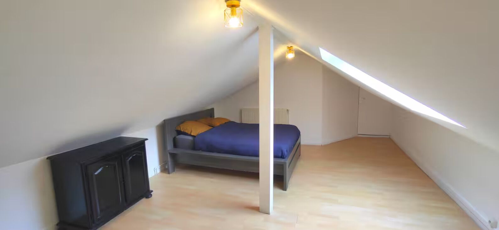 A small, sloped ceiling room with a bed, a black cabinet, and a skylight.
