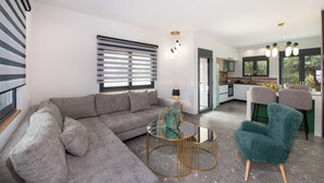 Ein modernes Wohnzimmer mit einem grauen Ecksofa, einem runden Couchtisch und einem smaragdgrünen Sessel.