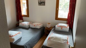 Une chambre avec deux lits, chacun étant muni d’un oreiller et d’une petite table de chevet. Il y a un tableau accroché au mur et une fenêtre avec des rideaux.