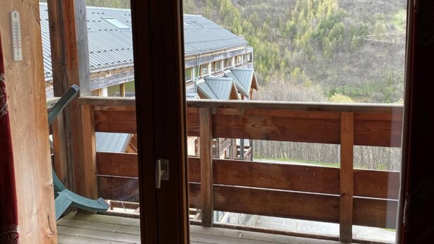Une terrasse en bois offrant une vue sur un immeuble et des collines boisées.