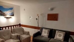 Un salon comprenant un canapé, un fauteuil à revêtement, une table en bois et un luminaire fixé au mur.
