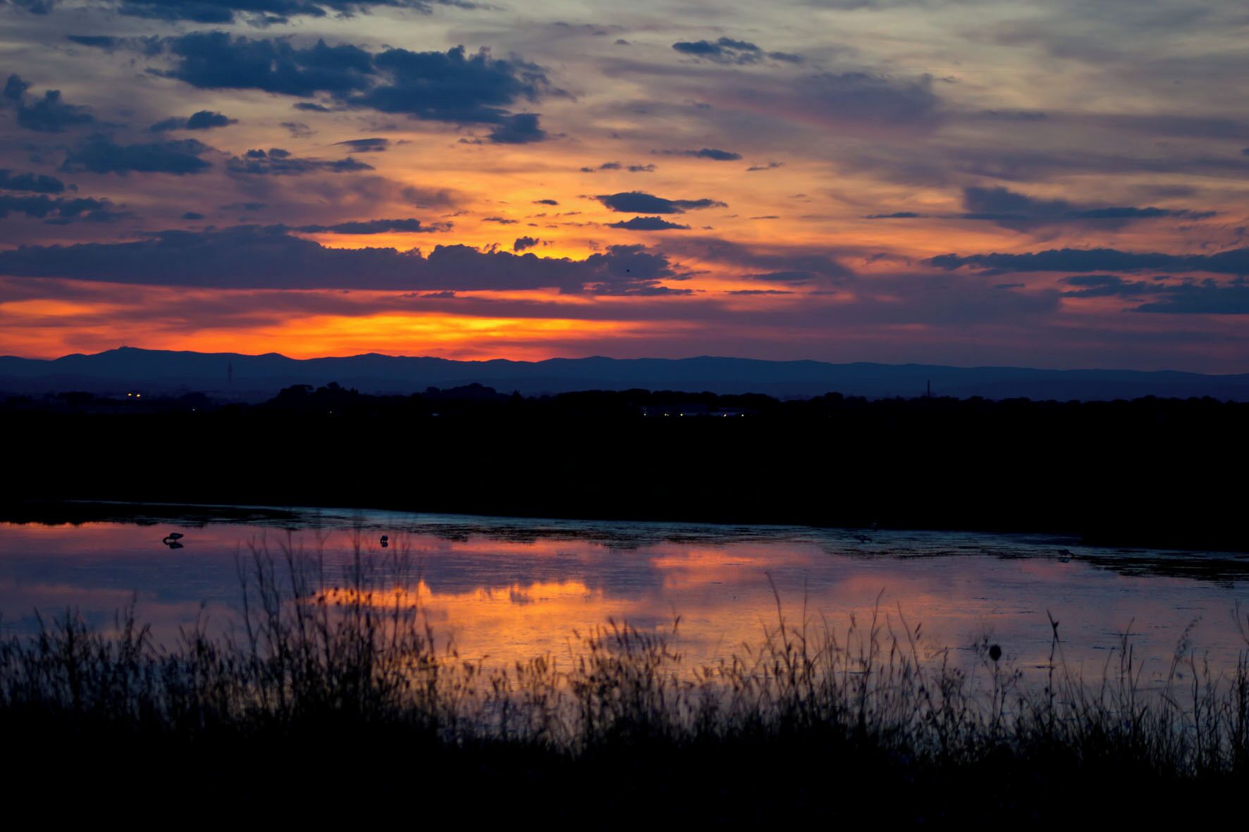 A sunset over a calm body of water with silhouettes of distant mountains and a flat horizon.