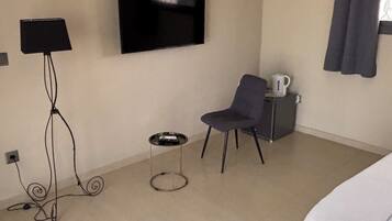 Hotelkamer met een bed, een aan de muur bevestigde televisie, een stoel, een klein tafeltje met een waterkoker en een raam met gordijnen.