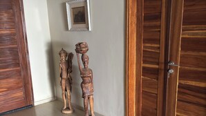 Une pièce avec une porte en bois, un tableau encadré au mur et deux sculptures en bois posées sur le sol.