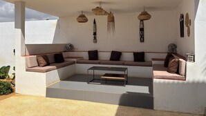 Un espace de détente extérieur moderne, comprenant un canapé modulable, des lampes suspendues en osier et des éléments décoratifs muraux.