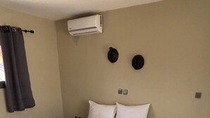 Une chambre à coucher comprenant un lit, un climatiseur, une petite table et deux éléments décoratifs fixés au mur.