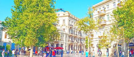 A public square with historic buildings, trees, and people.
