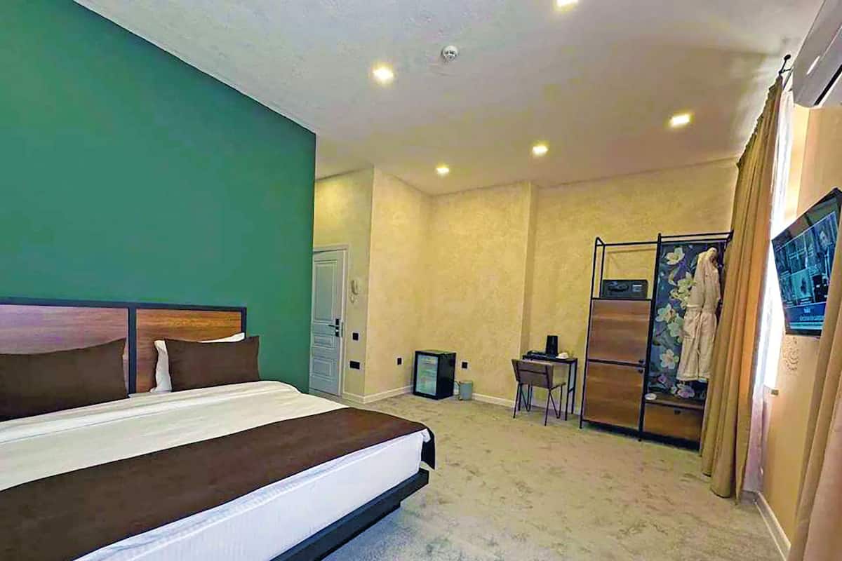 A hotel room with a large bed, a desk, a chair, a wardrobe, and a painting on the wall.